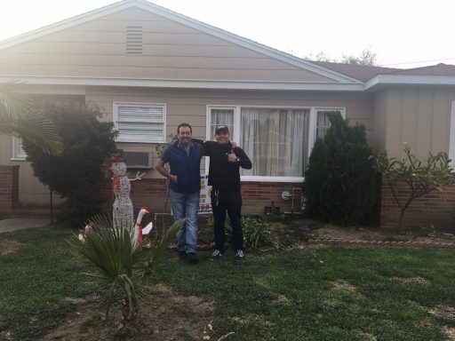 Another Happy Client Two men stand outside a house, posing near a small palm tree and garden area.